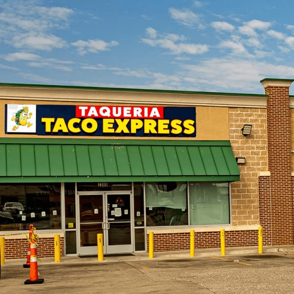 Exterior of Taqueria Taco Express with a green awning, brick facade, and a blue sky.