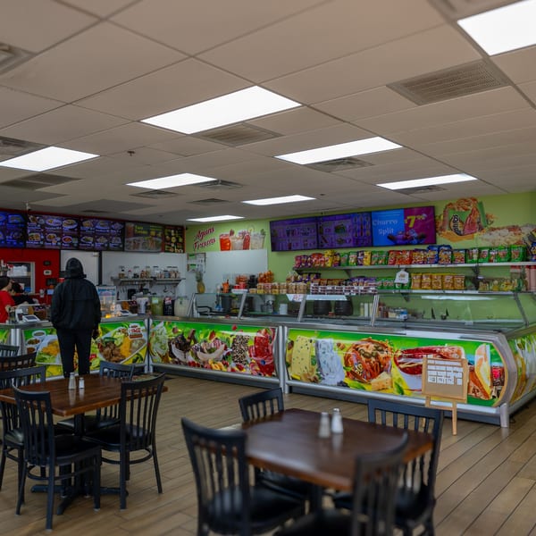 Interior of Taqueria Taco Express with a customer at the counter, menu boards, and empty tables.