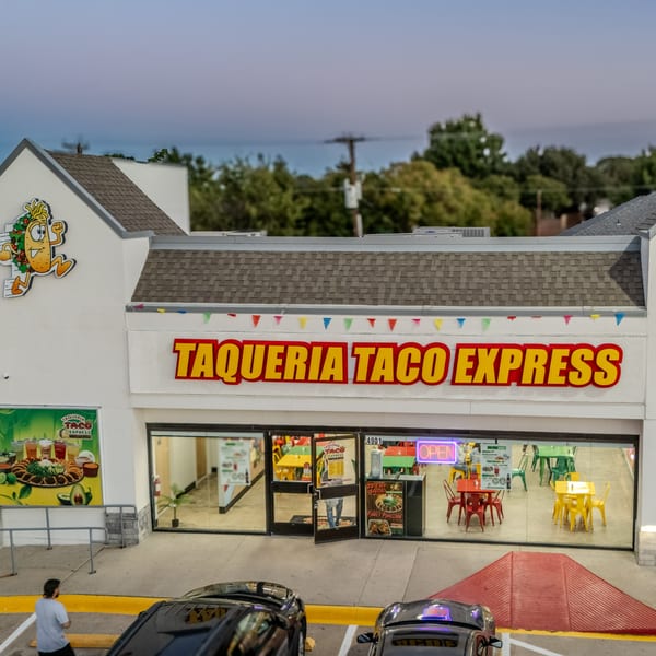 Exterior of Taqueria Taco Express with a bright sign, colorful interior, and cars parked outside.