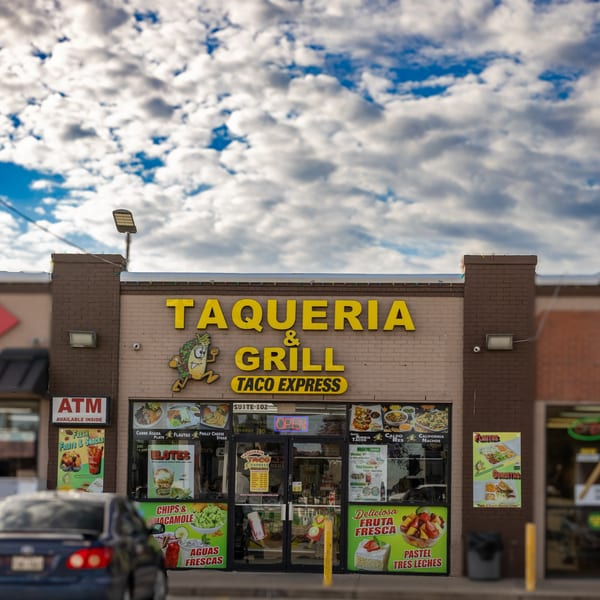 Exterior of Taqueria Taco Express with yellow signage, menu posters, and a blue car in front.