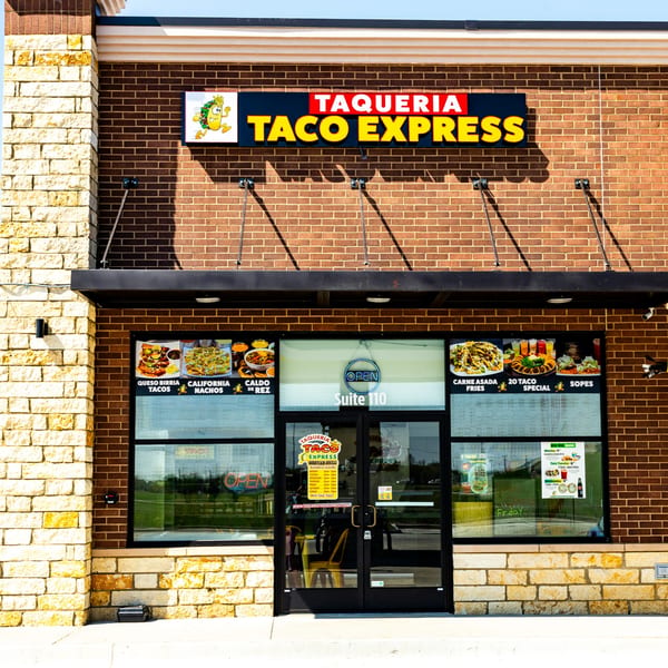 The exterior of Taqueria Taco Express, a Mexican restaurant with a brick facade and large windows.