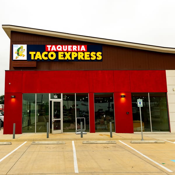 Exterior of Taqueria Taco Express with a red facade, large windows, and a parking lot.