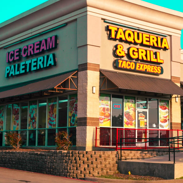 Exterior of Taqueria Taco Express and Ice Cream Paleteria with bright signs and window displays.