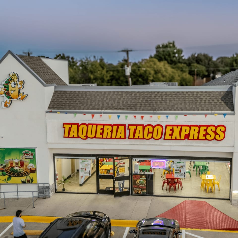 Exterior of Taqueria Taco Express with a large sign, colorful interior, and cars parked outside.